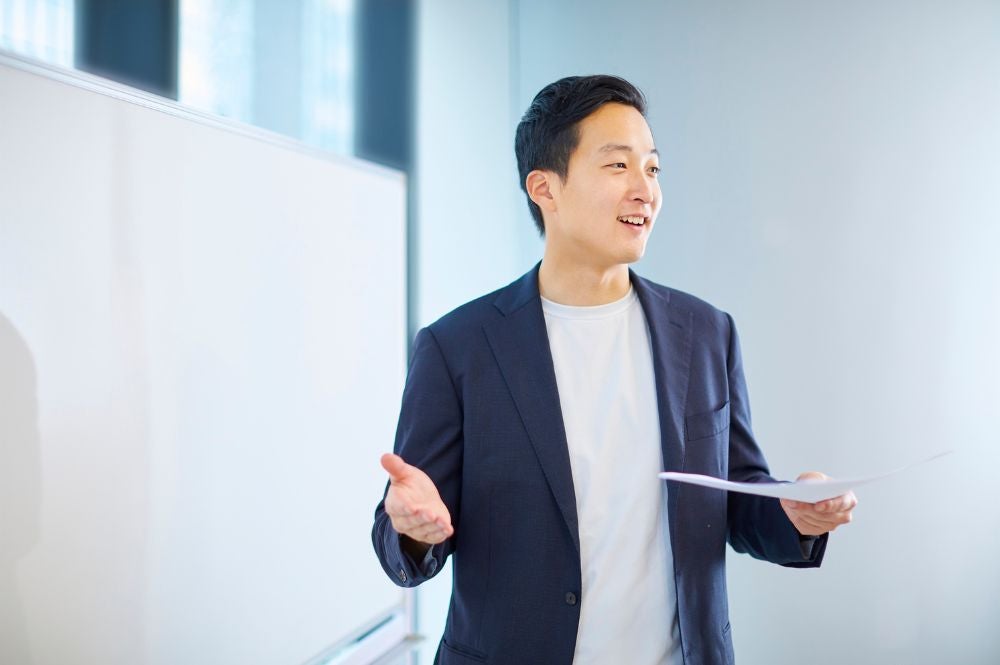  A young man in a suit stands by a whiteboard, discussing business English for professionals.