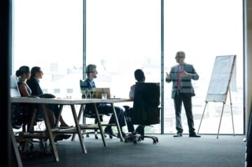 A man stands in front in a corporate meeting room employees while teaching a corporate English training course