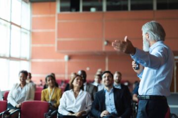 A business English instructor stands in front of a group of corporate employees teaching them the basics of business communication.