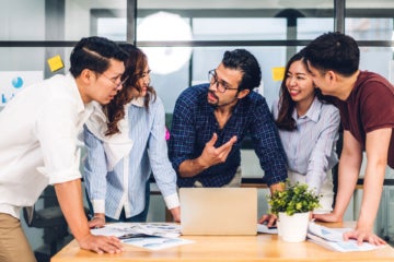 Working professionals huddled together in front of a laptop