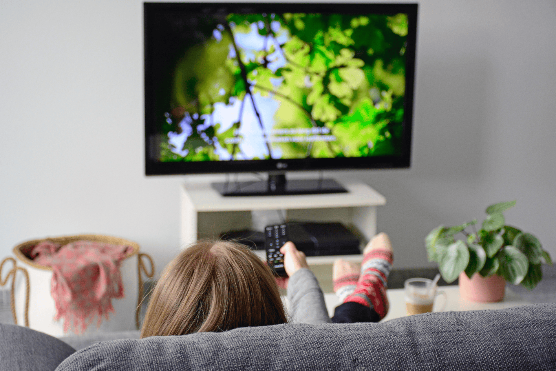 A young woman watching TV on a gray couch with subtitles