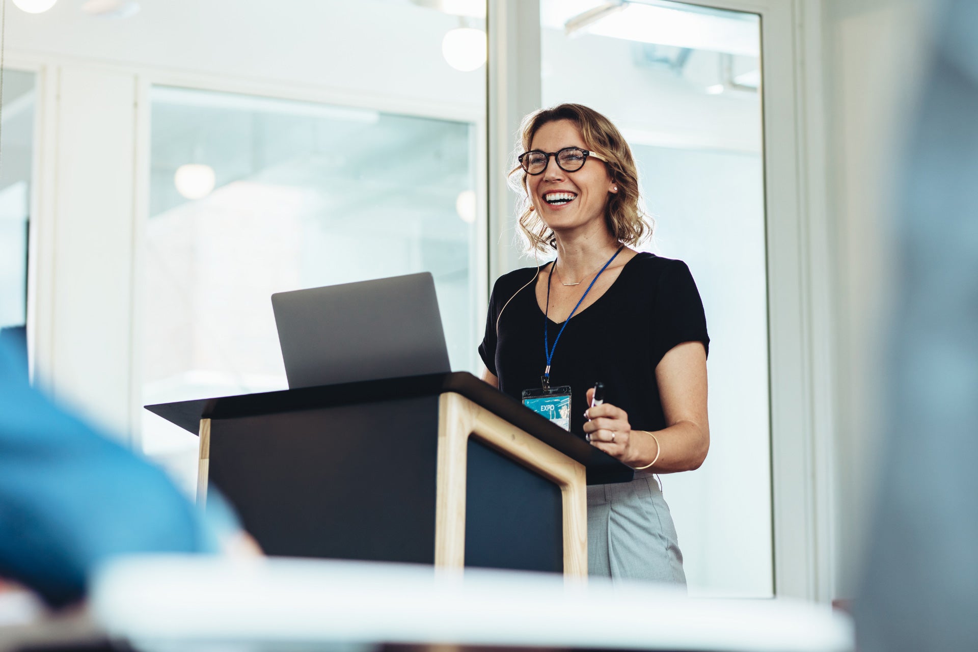 A business professional at a podium with windows behind her doing a presentation