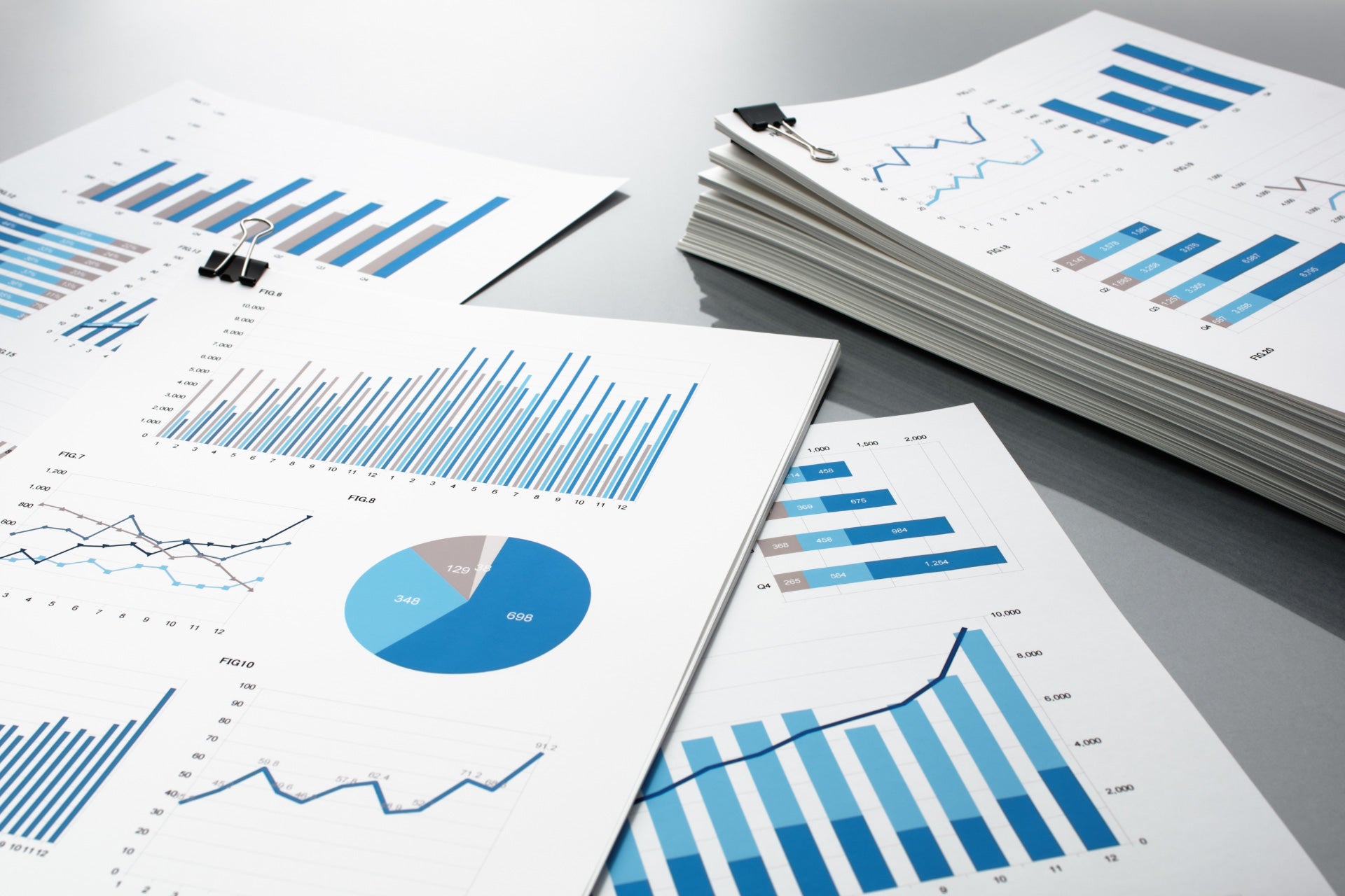 Business reports and a pile of documents with charts and graphs on gray reflection background