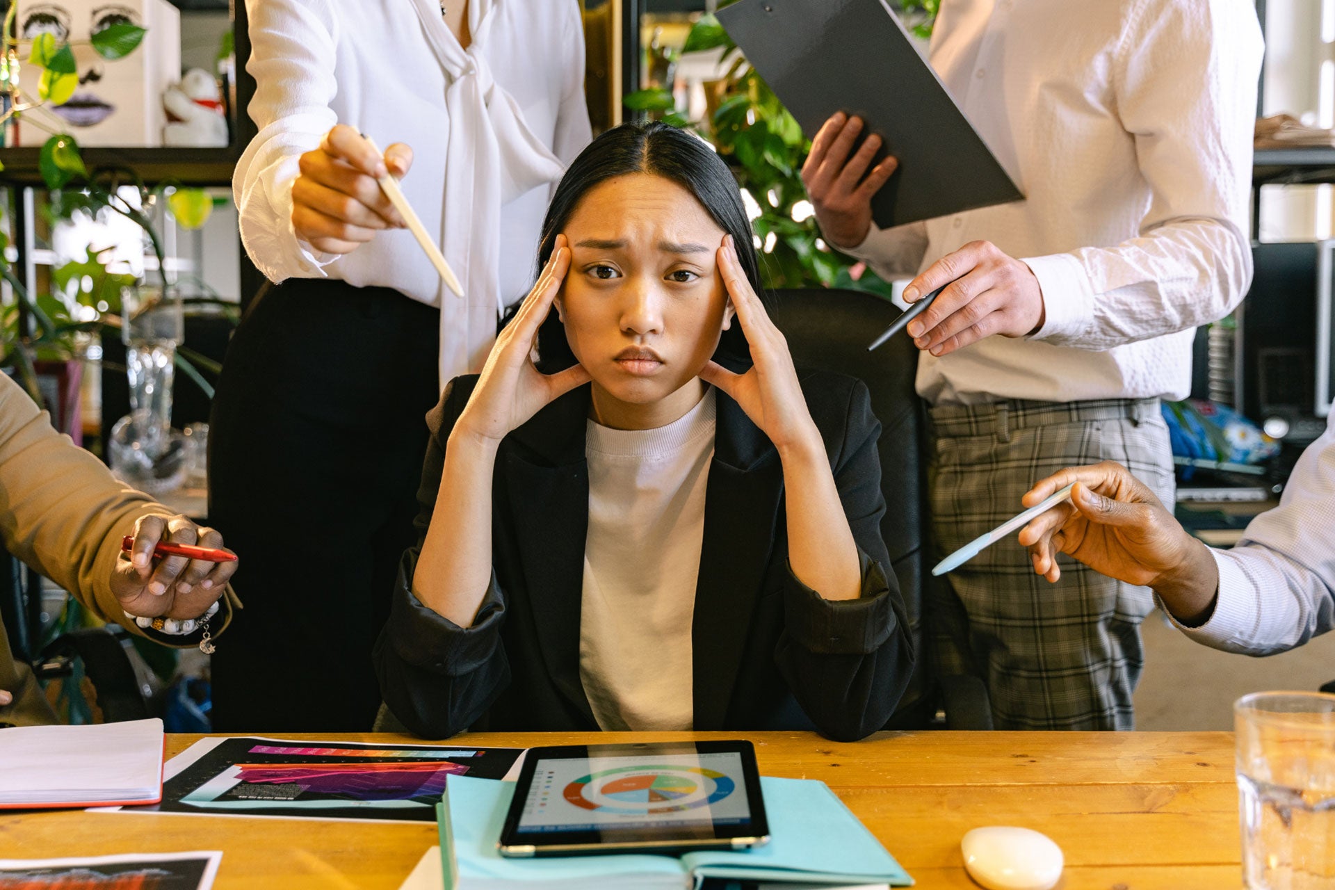 A businesswoman sitting in a chair looking stressed while other people point pens at her