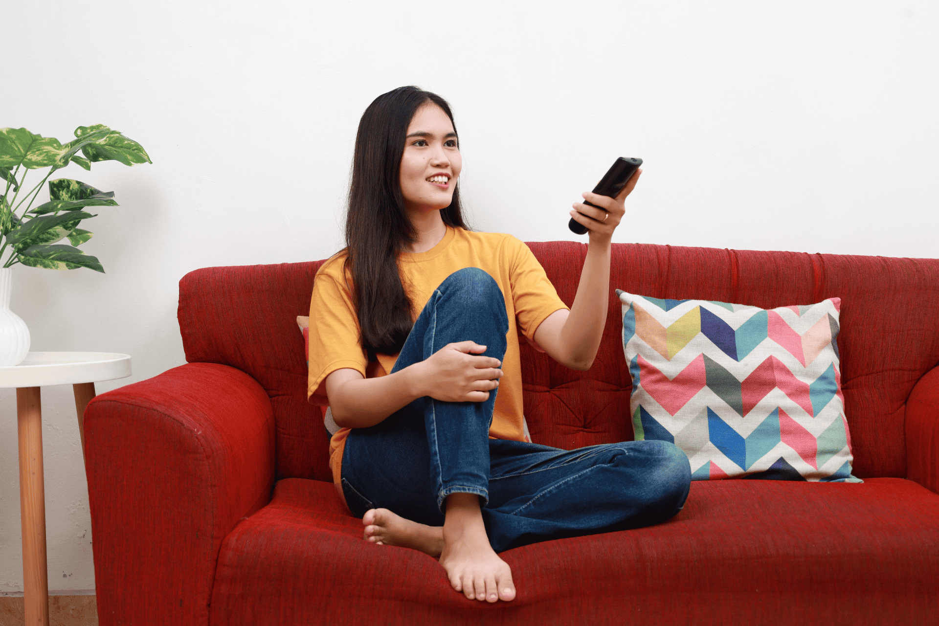A woman sitting on a red couch holding a TV remote